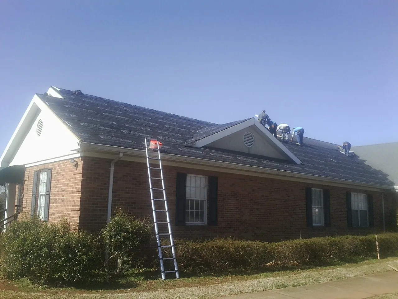 Crew tearing shingles off a brick ranch roof with a ladder set — Metal Roof Repair work by our crew in Monee