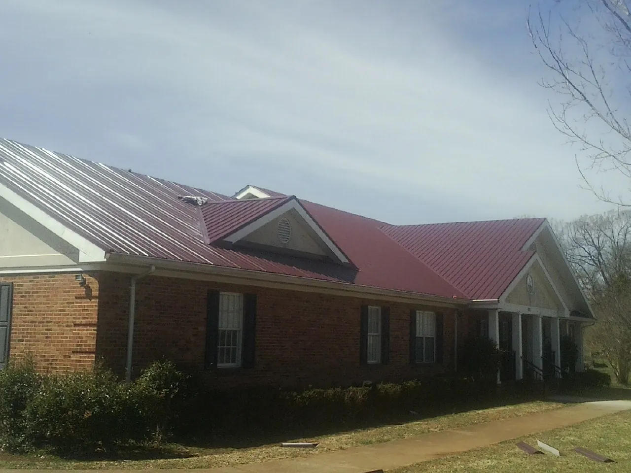 Red metal roof with gabled entries on a long brick building, from a Hail Damage Roof Repair job in Monee