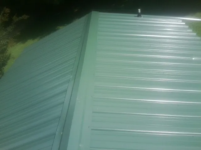 New green metal panels meeting at the ridge of a roof — Flat Roof Repair work by our crew in Monee