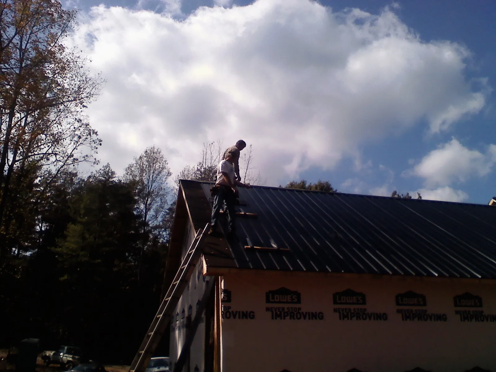 Roofer fastening dark metal panels high against a cloudy sky, from a Roof Inspection job in Monee