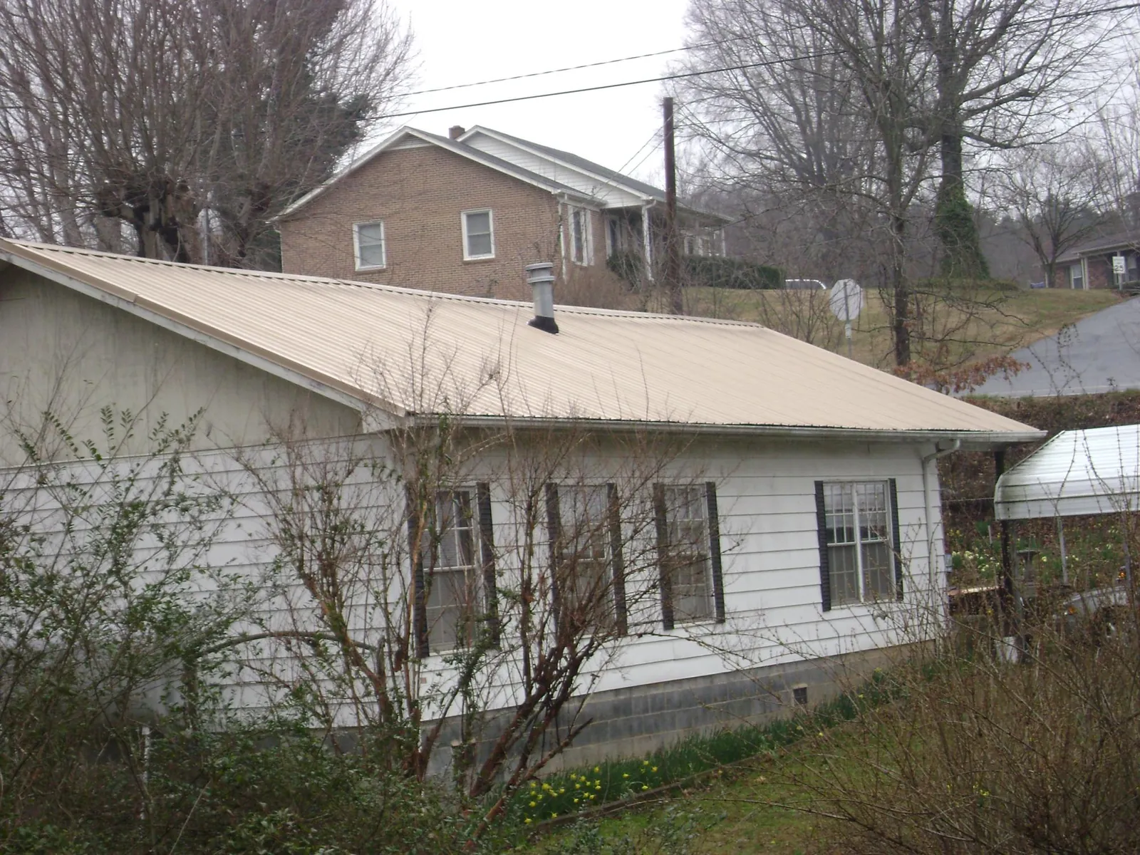 Tan metal roof on a white sided house set into a hillside — Commercial Roofing by Roofing Brothers in Monee